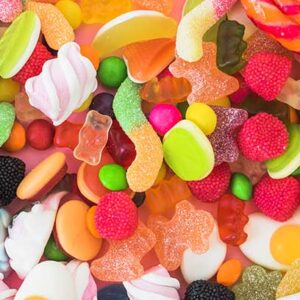 Variedad de dulces coloridos y gomosos sobre un fondo rosa, incluyendo ositos de goma, caramelos, gomitas en forma de huevo, y otras golosinas. Ideal para amantes de los dulces y fiestas.